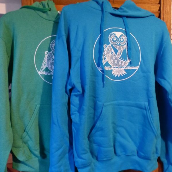 Both our green and blue Hessilhead hoodies hanging up showing the front of the jumper with our logo